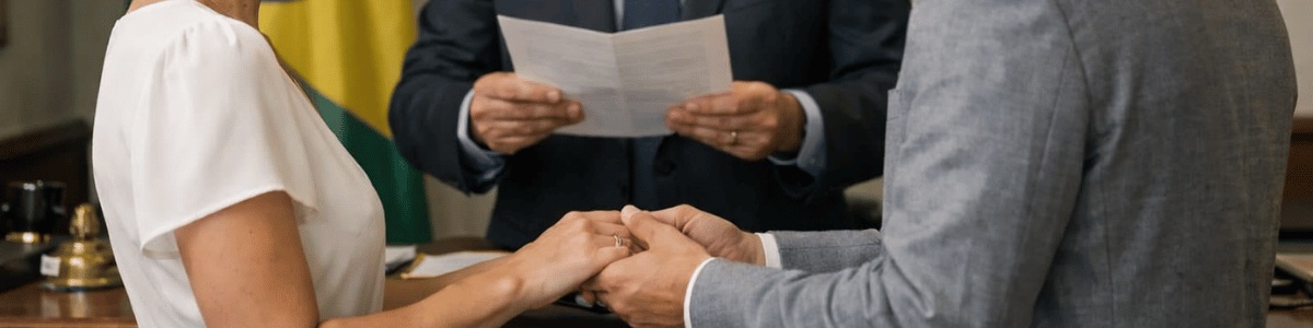 um casamento civil em um consulado, com o casal de frente um para o outro, trocando olhares e segurando as mãos, enquanto o funcionário consular conduz a cerimônia