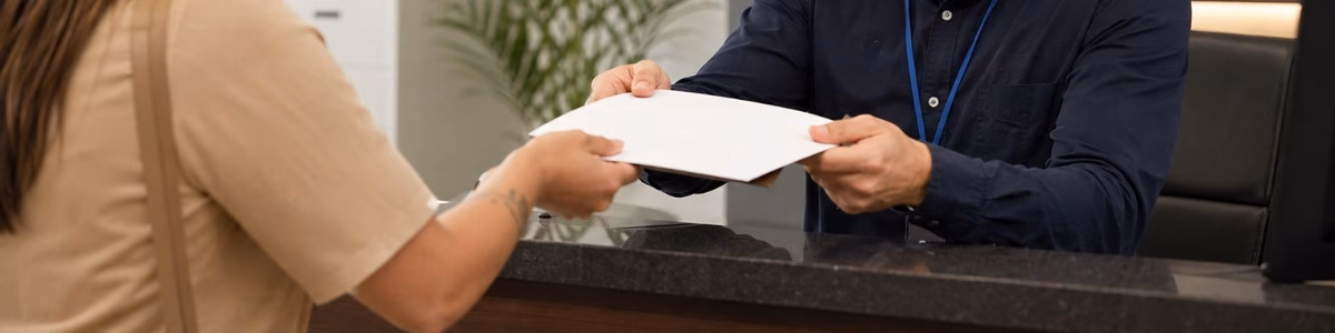 Pessoa recebendo uma certidão diretamente de um atendente no balcão de um cartório, em um ambiente profissional, organizado e com atendimento cordial