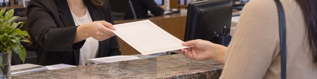 certidão inteiro teor DF Funcionária de cartório entrega uma certidão a uma cliente durante atendimento presencial, em um ambiente profissional, organizado e acolhedor
